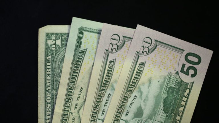 quatro notas de dólar uma ao lado da outra, em formato de leque, num fundo preto