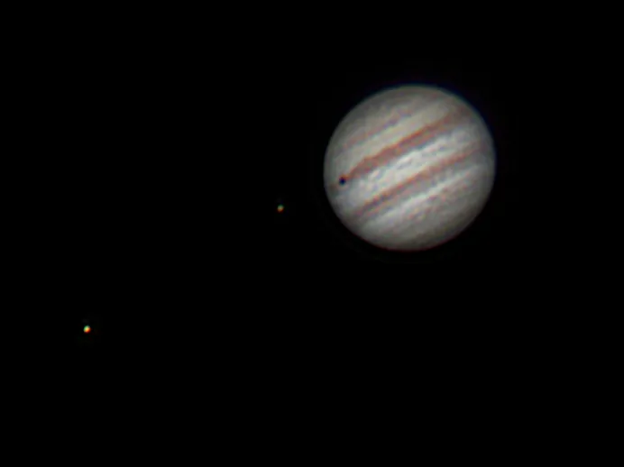 Юпитер и два спутника, один из которых отбрасывает тень на его поверхность.