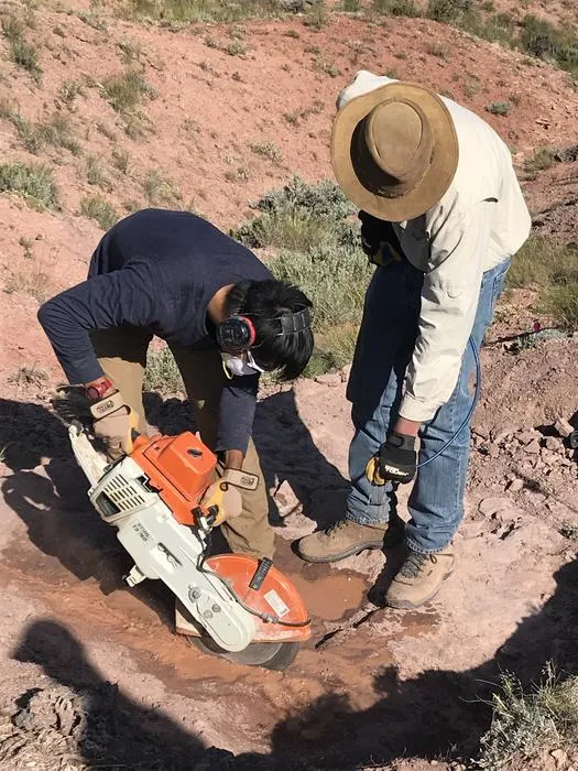 два человека работают оранжево-белой пилой в красной скале